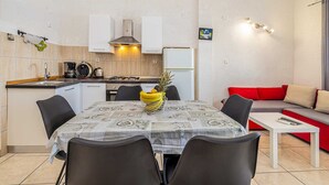 A compact kitchen with a dining table, chairs, a red sofa, and a small white table. - Apartment STARA BAŠKA with sea view (Stara Baška)