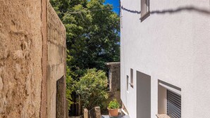 A narrow alleyway with a white building on the right, a stone wall on the left, and a potted plant in the center. - Apartment STARA BAŠKA with sea view (Stara Baška)