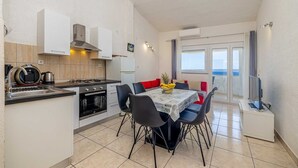 A compact kitchen with modern appliances, a dining area with a table and chairs, and a balcony with a view. - Apartment STARA BAŠKA with sea view (Stara Baška)