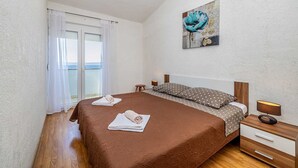 A bedroom with a large bed, a nightstand, a lamp, and a painting on the wall. - Apartment STARA BAŠKA with sea view (Stara Baška)