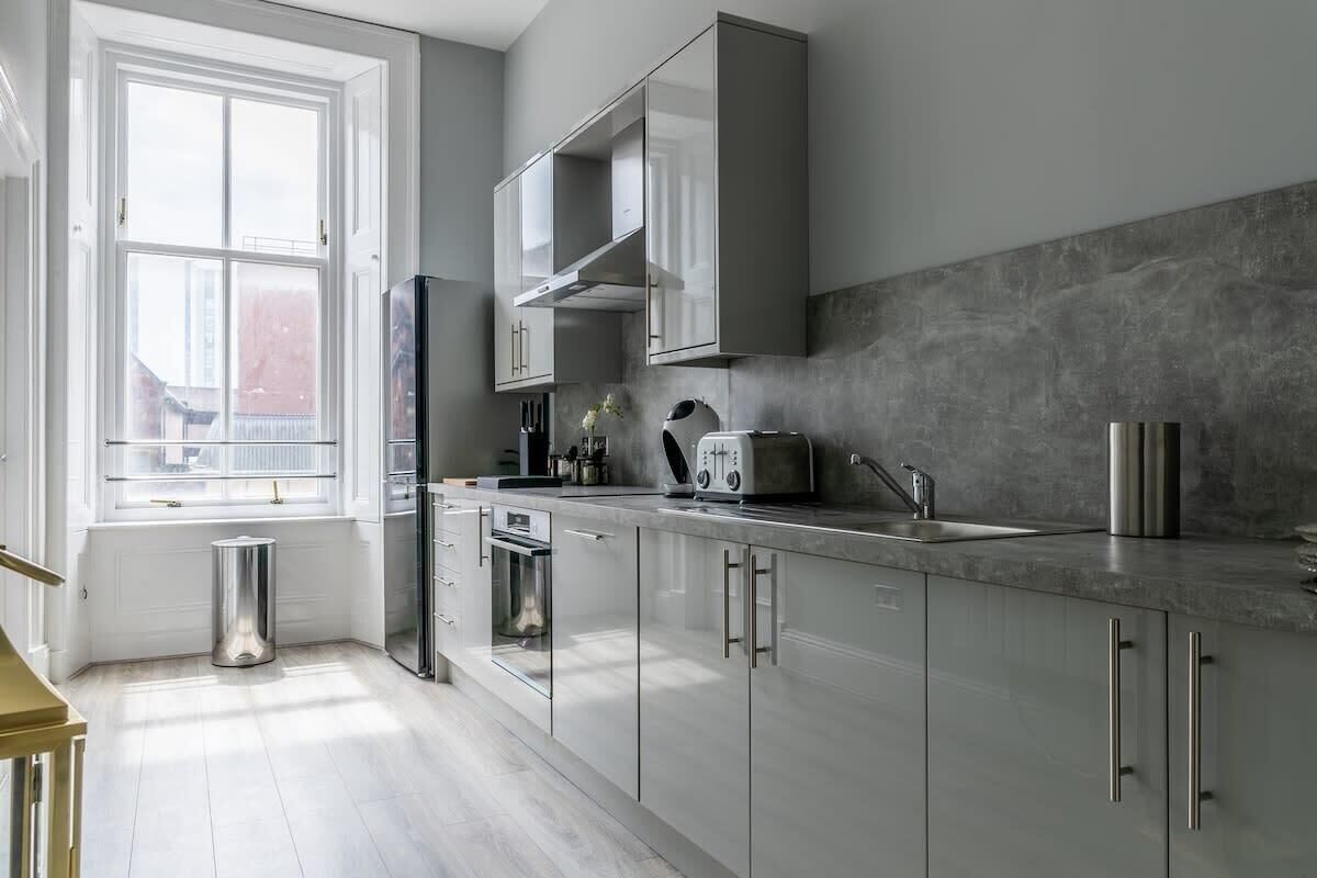 A modern kitchen with a large window, stainless steel appliances, and a grey backsplash.