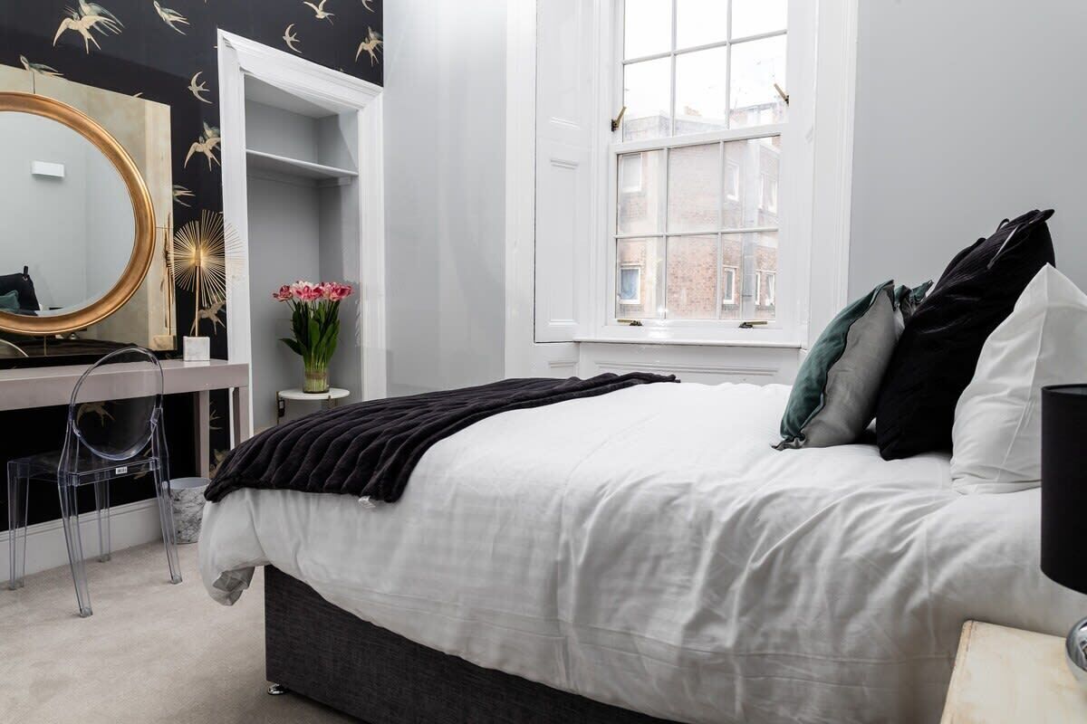 A bedroom with a bed, a dresser, a mirror, and a window.