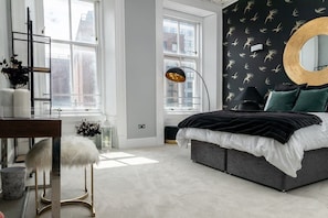 A modern bedroom with a large bed, a desk, and a chair. There are windows, a mirror, and a lamp. - Modern 4-Bedroom City Retreat in Glasgow (Glasgow City)