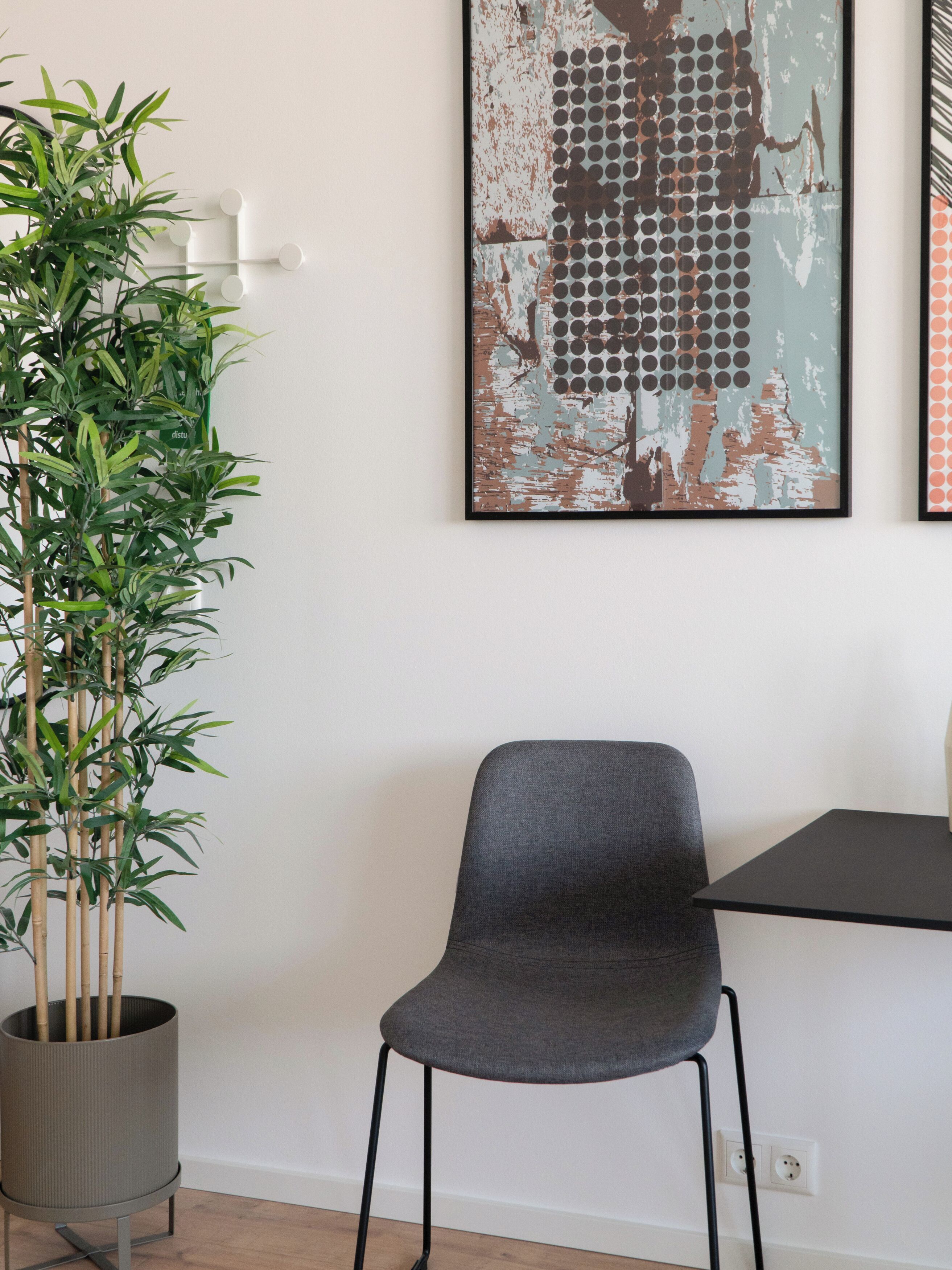 Une pièce avec un fauteuil gris, une plante en pot et un mur orné d’une œuvre d’art à la texture particulière.