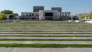 Un bâtiment moderne doté d’un toit plat et de grandes fenêtres, entouré d’une pelouse bien entretenue et agrémenté d’un chemin piétonnier au motif décoratif.