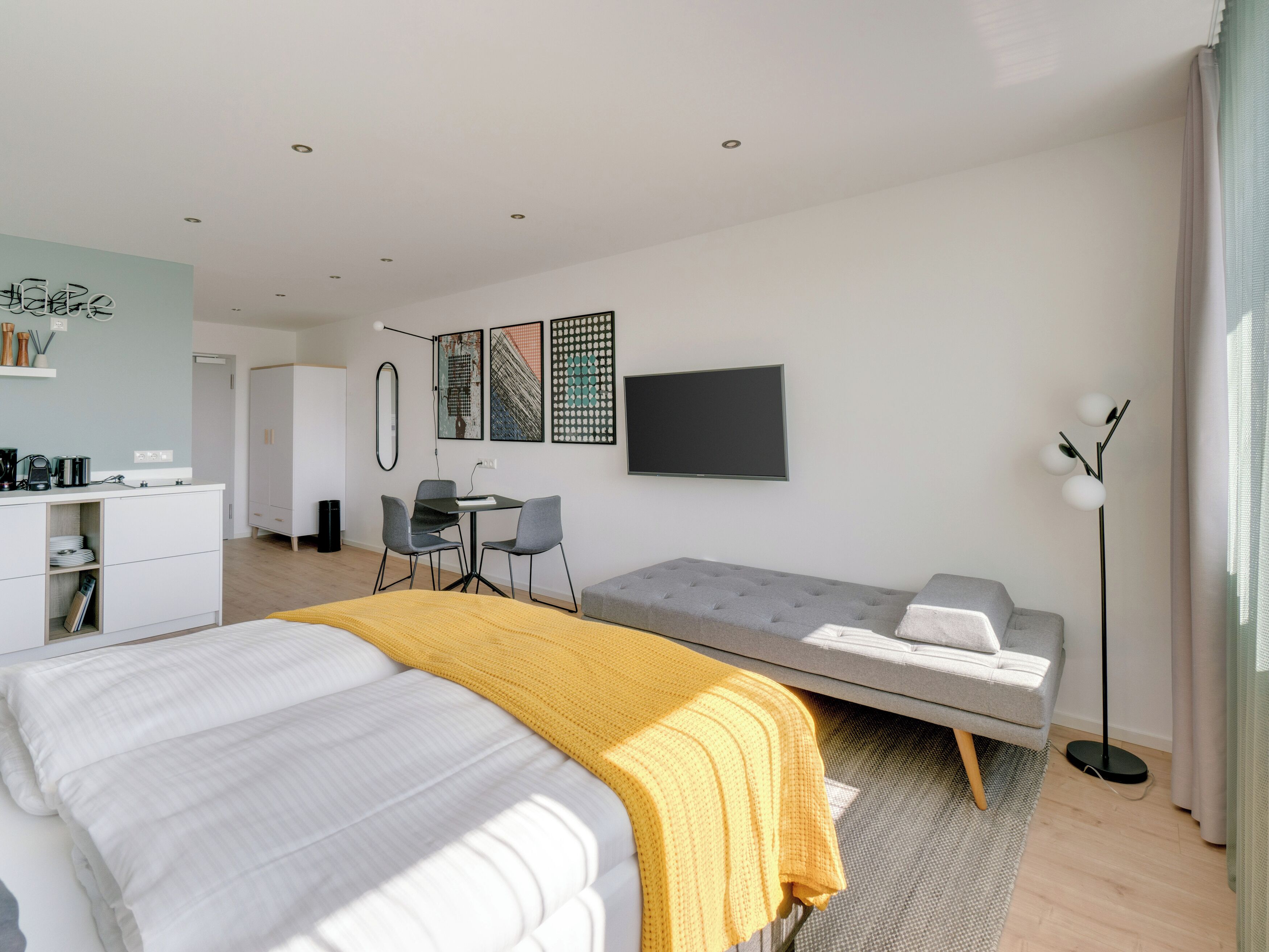 Una camera d'albergo moderna con un letto, una poltrona, una scrivania con sedie, una TV a schermo piatto e opere d'arte alle pareti.