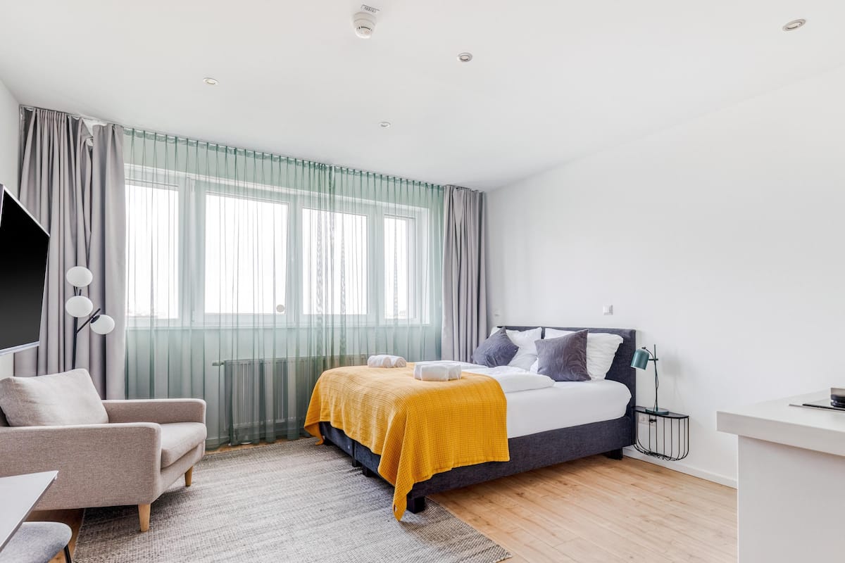 Une chambre moderne avec un lit, une chaise, un bureau et une grande fenêtre avec des rideaux.