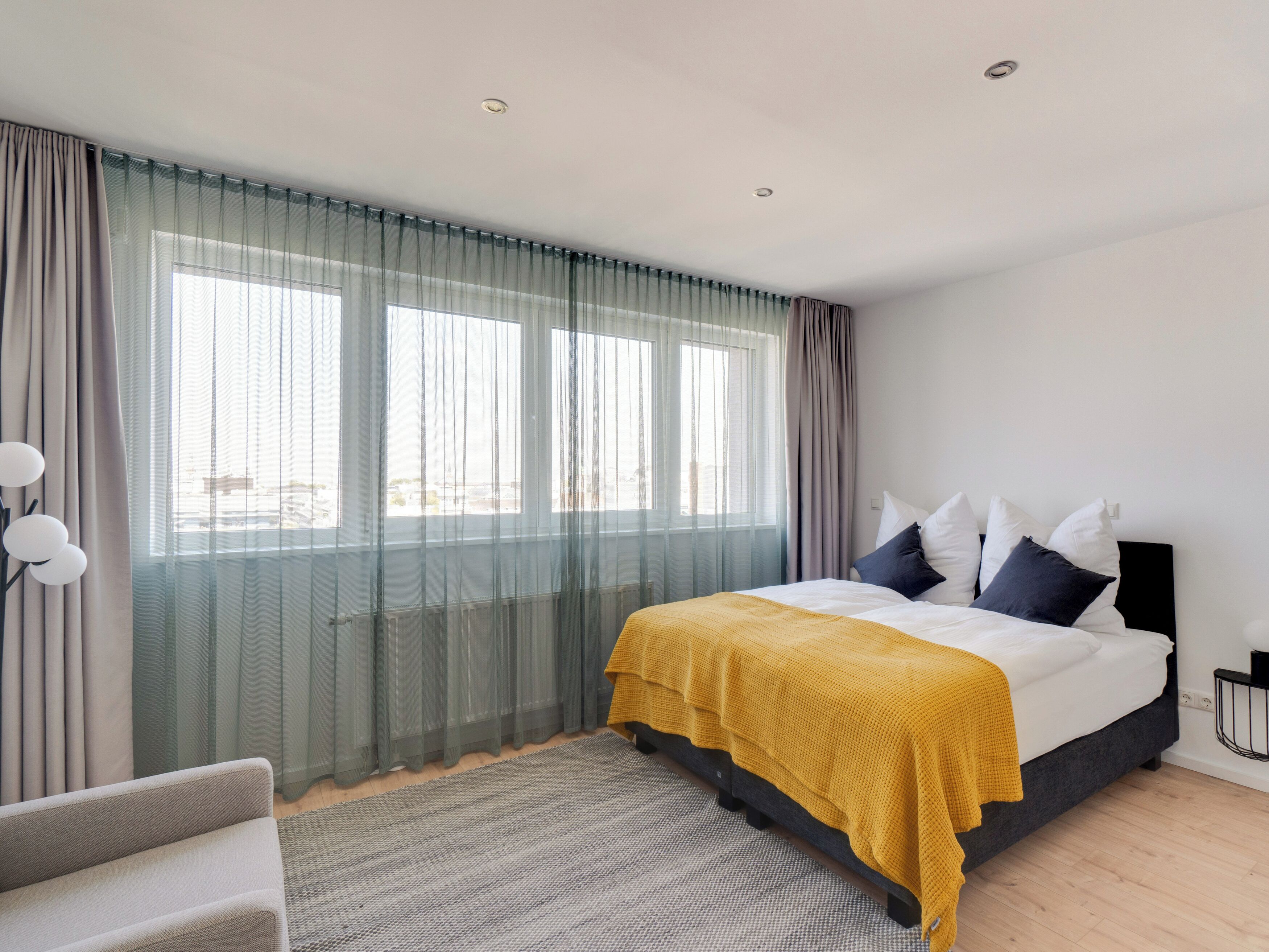 A modern bedroom with a bed, curtains, a chair, and a view through the window.