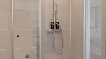 A modern shower with a glass enclosure, a handheld showerhead, and two bottles of shampoo on a shelf.
