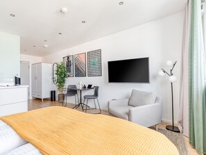 Ein modernes Hotelzimmer mit Bett, Schreibtisch, grauem Sofa und einem großen Fenster.