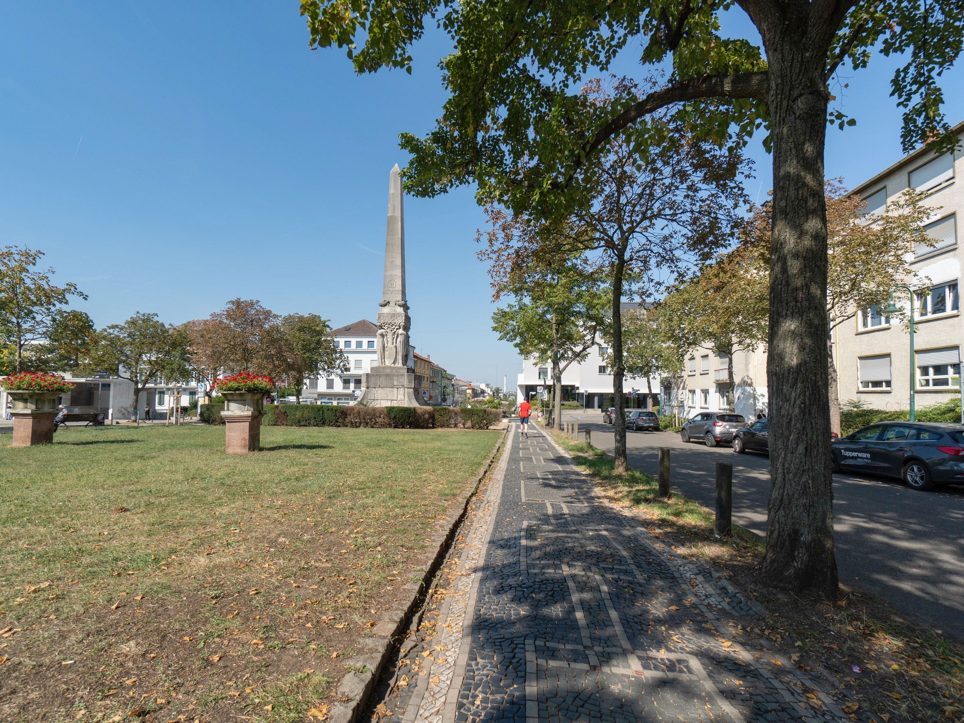 Un camino pavimentado con un monumento a lo lejos, rodeado de árboles y edificios.