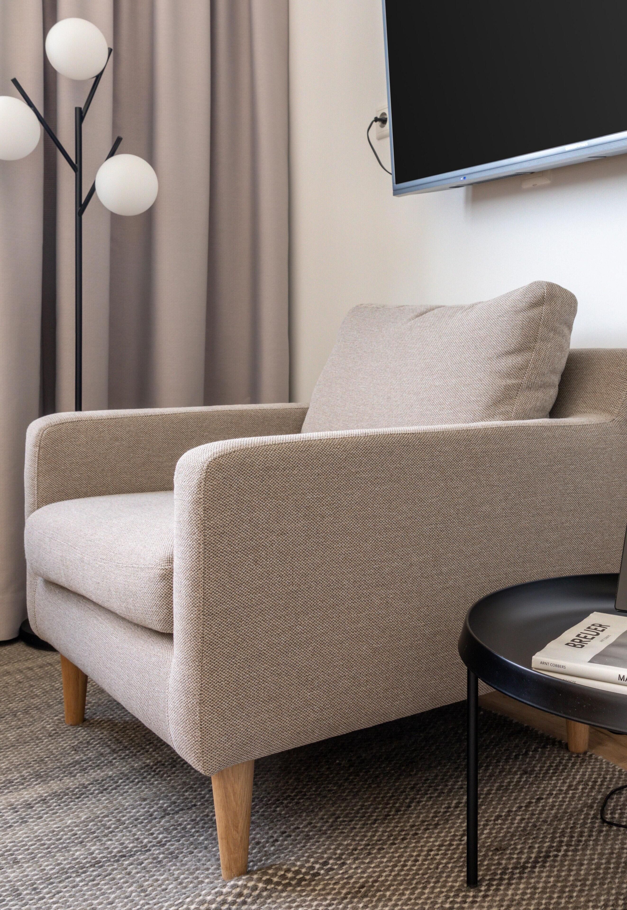 A modern living room with a beige armchair, a round black side table, and a floor lamp.