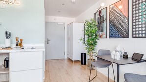 Une cuisine moderne avec des meubles blancs, un plan de travail en bois et un coin repas comprenant une table et des chaises. On y trouve également une plante en pot et des œuvres d’art accrochées aux murs.