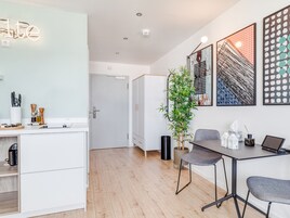 Una cocina moderna con armarios blancos, encimera de madera y comedor con mesa y sillas. Hay una planta en maceta y obras de arte en las paredes.