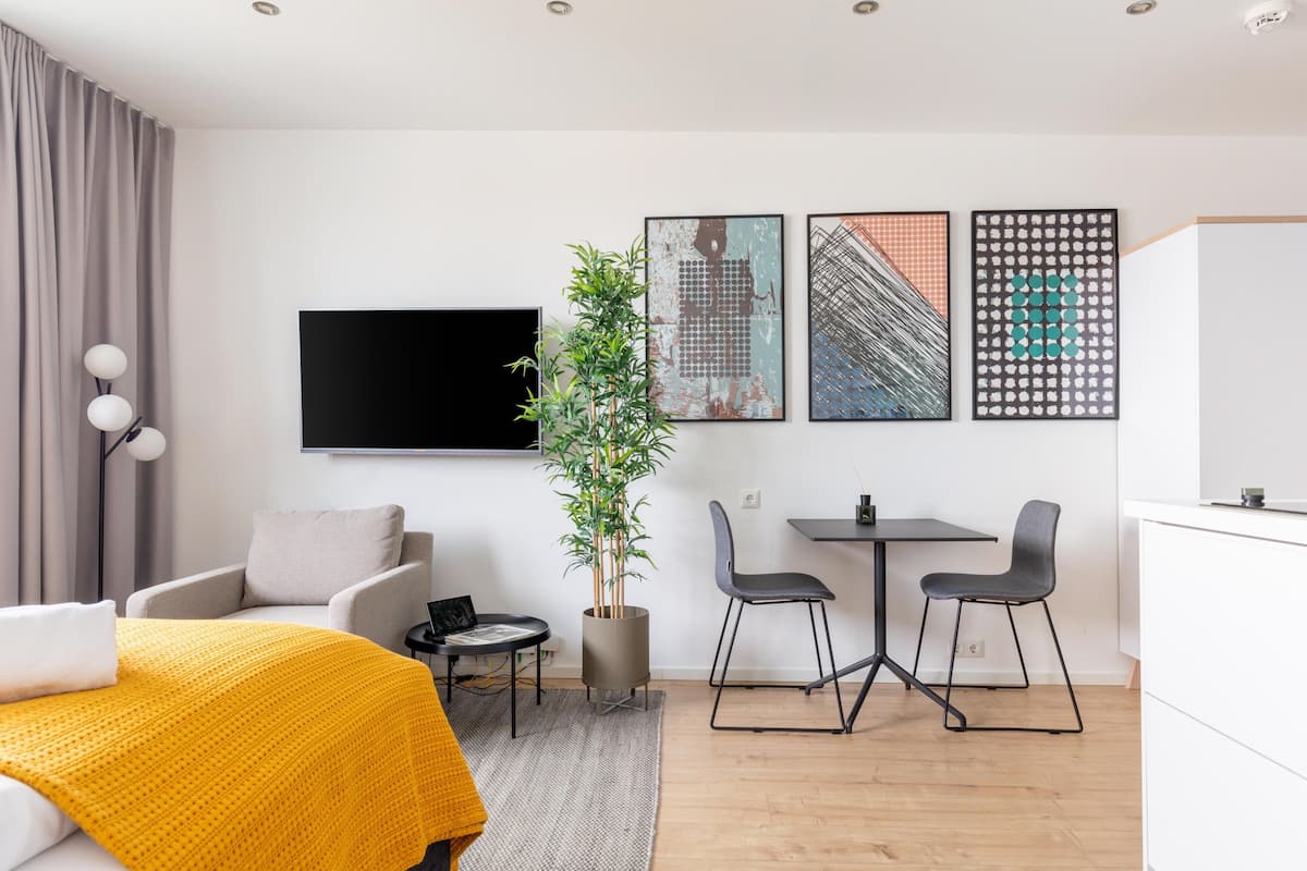Une chambre d’hôtel moderne, équipée d’un lit, d’un bureau, de deux chaises, d’une plante en pot et d’œuvres d’art accrochées au mur.