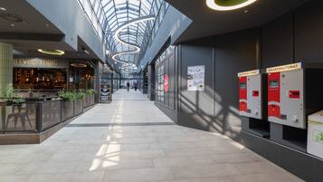 A modern indoor space with a high ceiling and skylights, featuring a restaurant, trash bins, and a clear walkway.