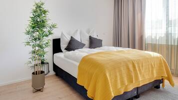 A modern bedroom with a bed, a potted plant, and a view of the outside.