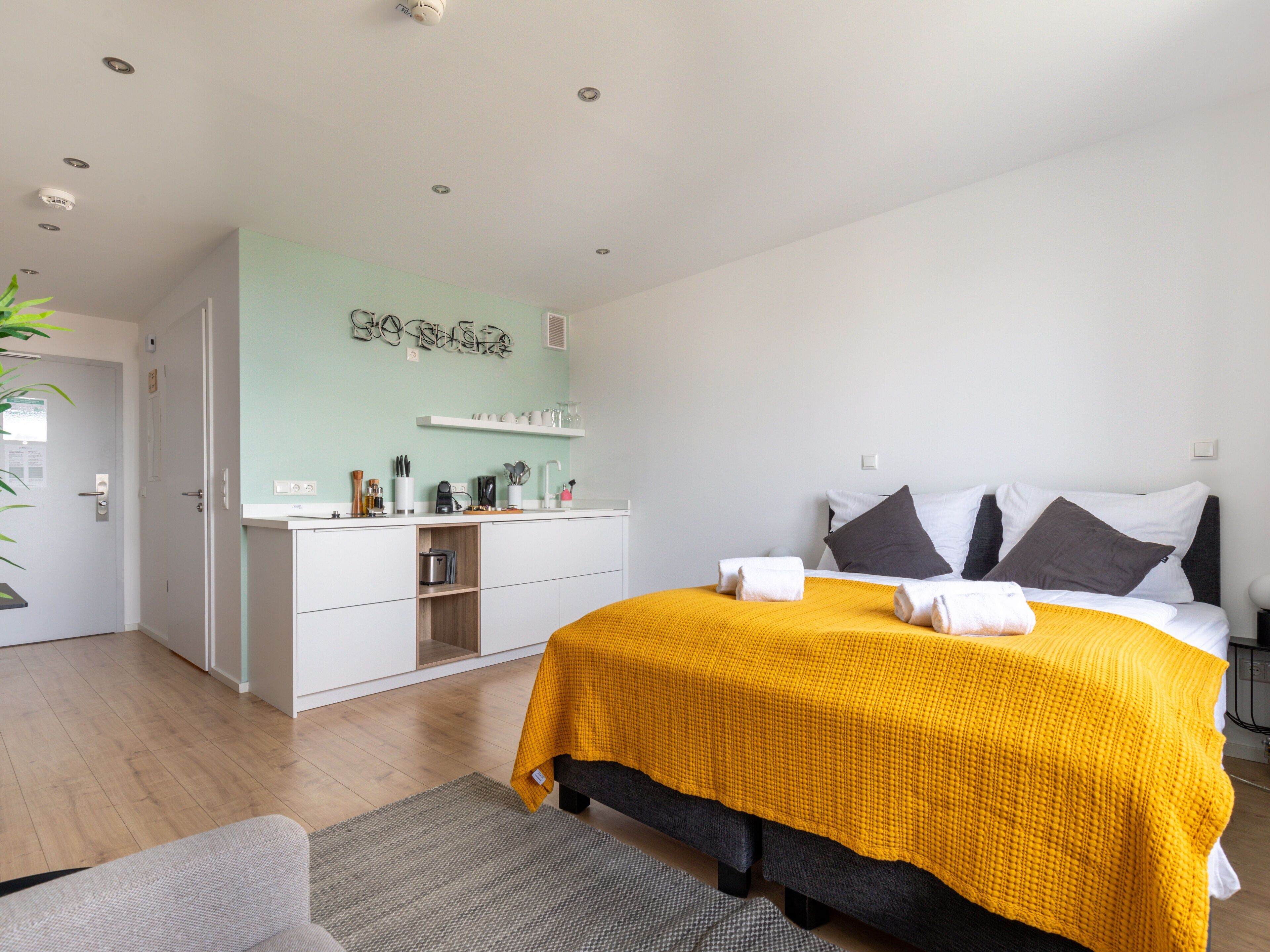 Un dormitorio moderno con cama, mesitas de noche, un armario y una cocina equipada, además de una pared verde.