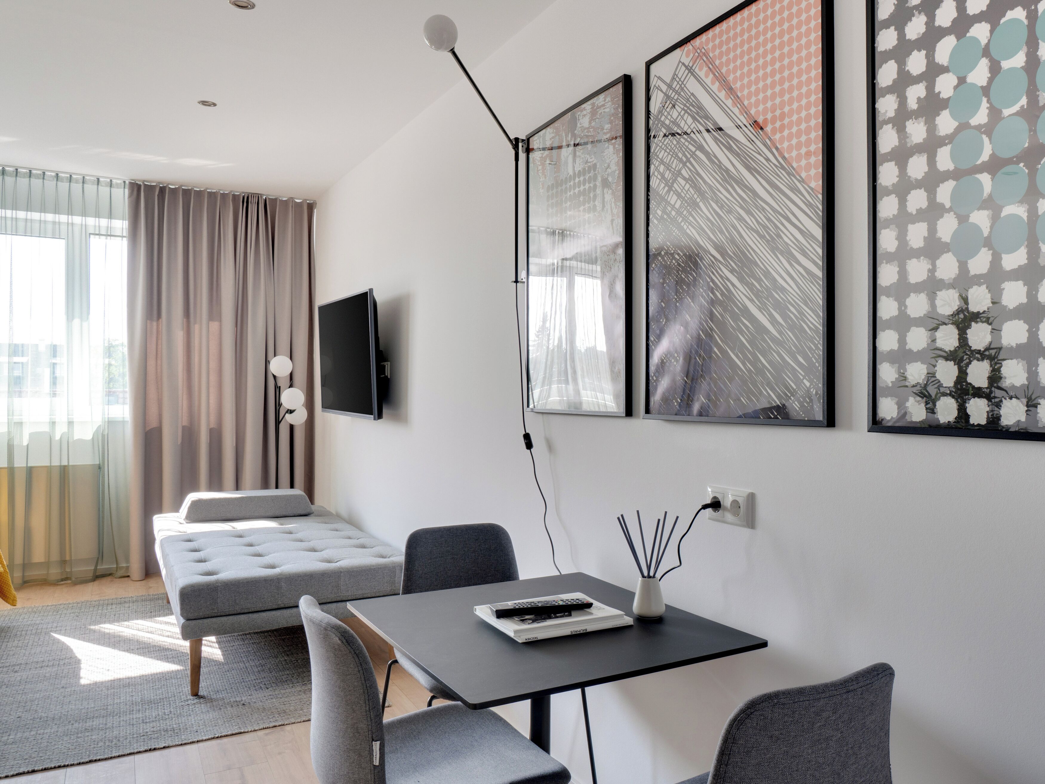 Una habitación de hotel moderna con una cama, un escritorio con silla, un televisor montado en la pared y obras de arte.