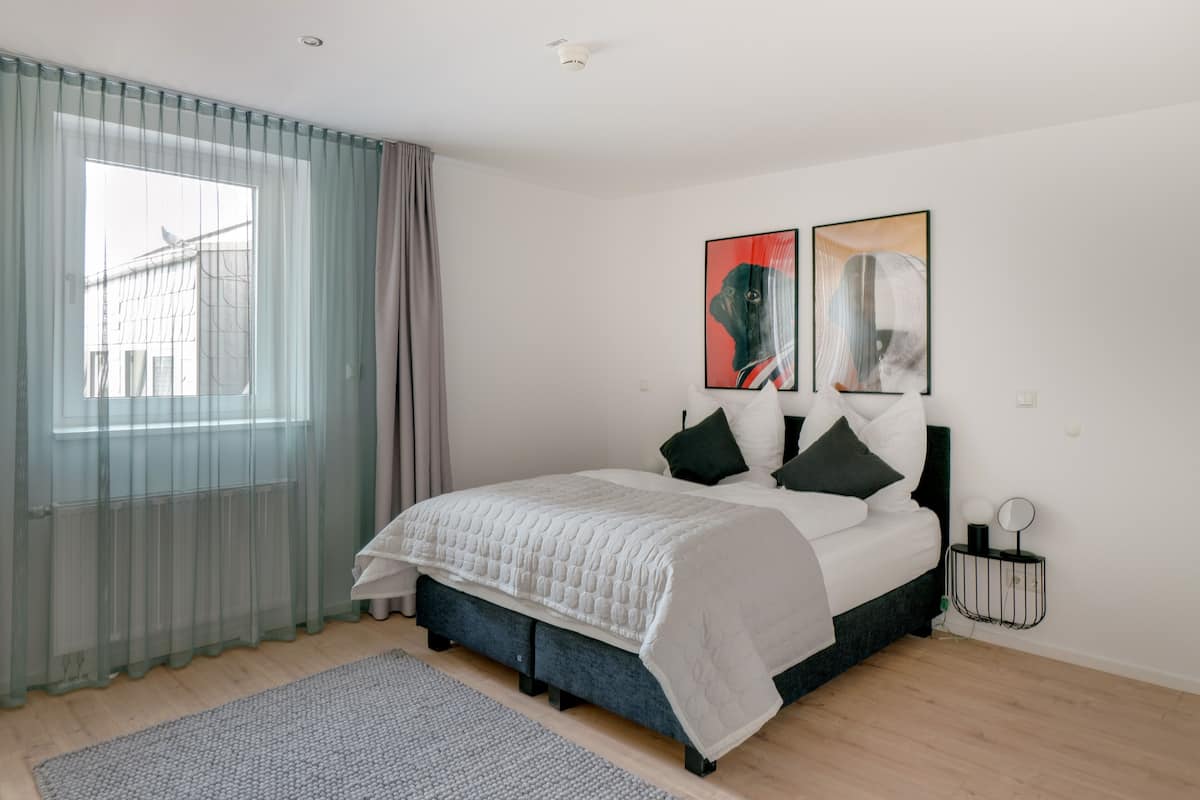 Une chambre à coucher moderne avec un lit, une table de chevet, un tapis et des œuvres d’art accrochées au mur.
