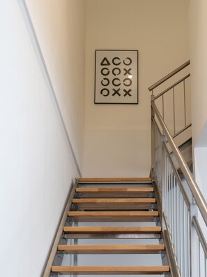 Eine Treppe mit Holzdielen und Metallgeländern, die zu einer Zwischenebene mit einem an der Wand befestigten Kunstwerk führt.