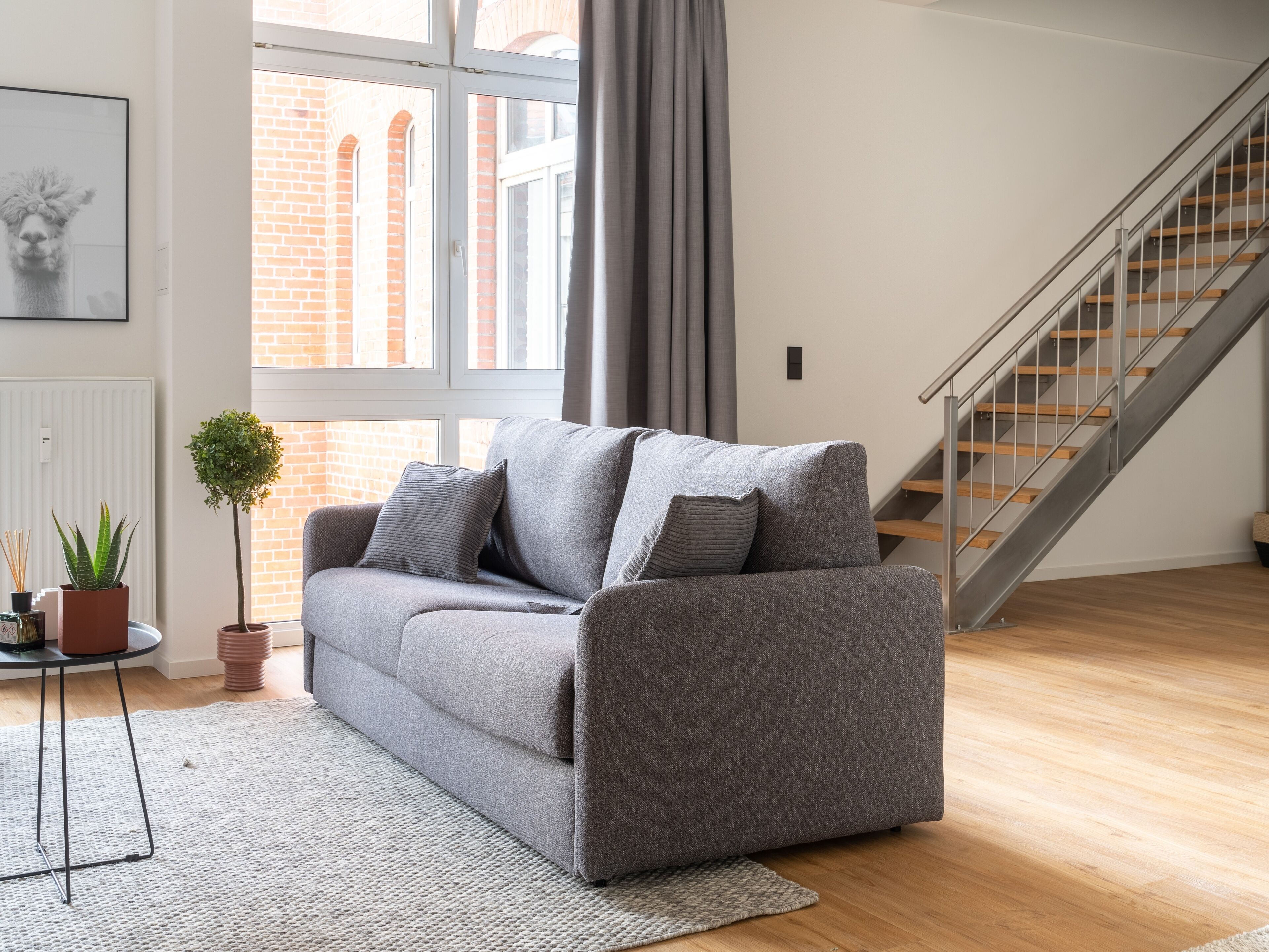 A modern living room with a grey sofa, a small potted plant, and a staircase.
