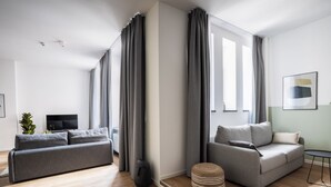 Una sala de estar moderna con un sofá gris, un otoman pequeño y redondo, y un televisor de pantalla plana.