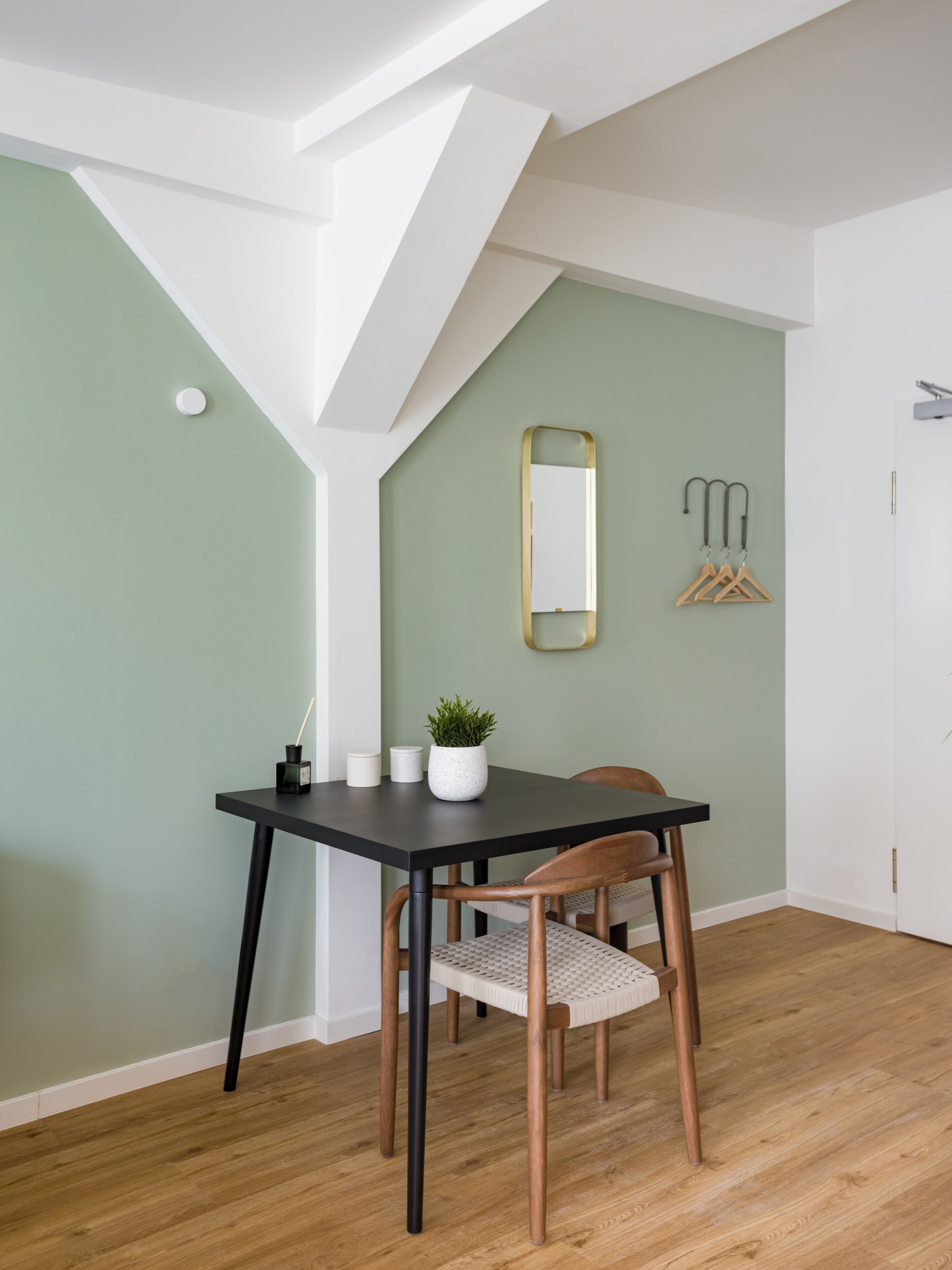 A dining area with a table and chairs, a potted plant, and a mirror on the wall.