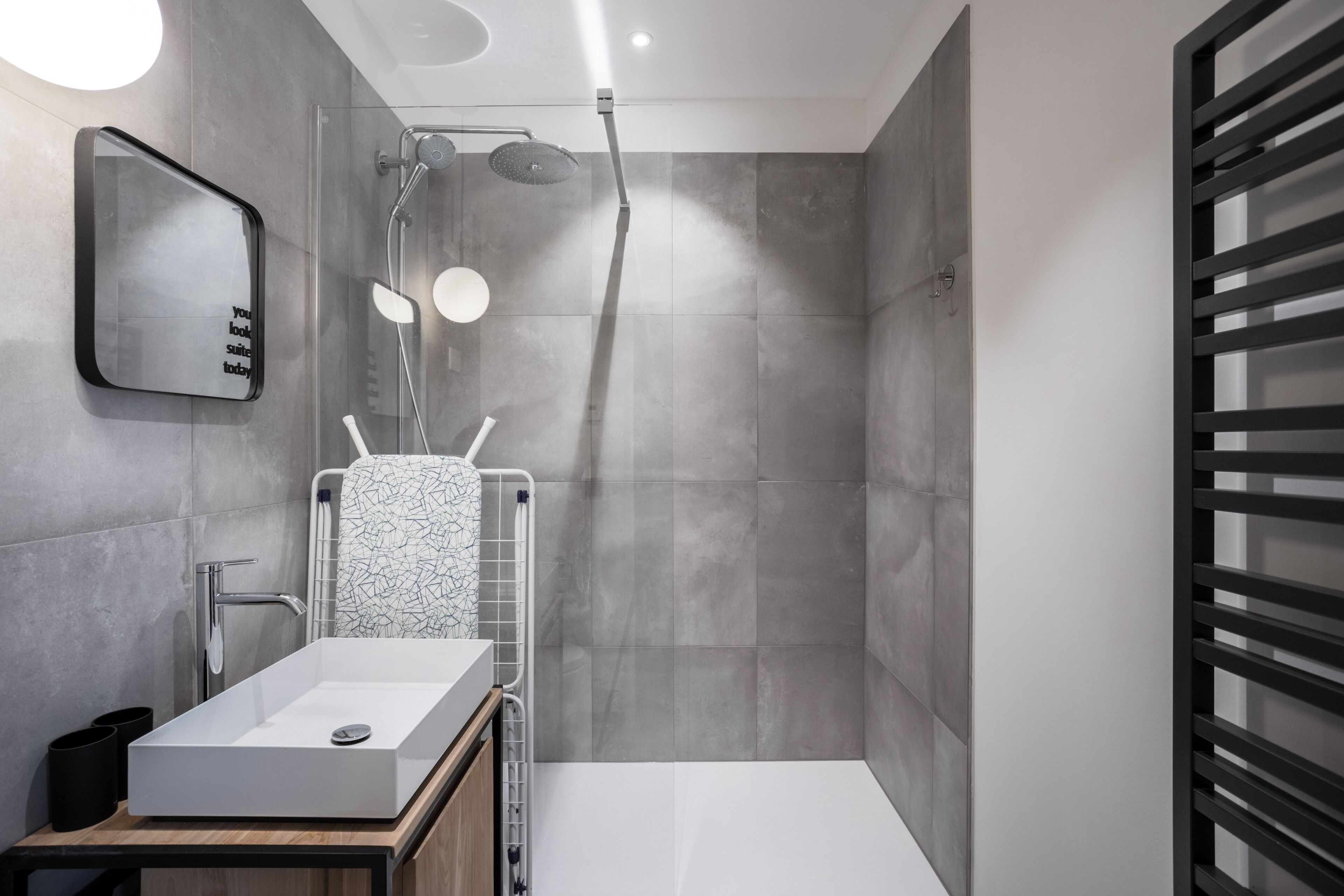 A modern bathroom with a large rectangular sink, a shower with a glass door, and a towel rack with a patterned towel.