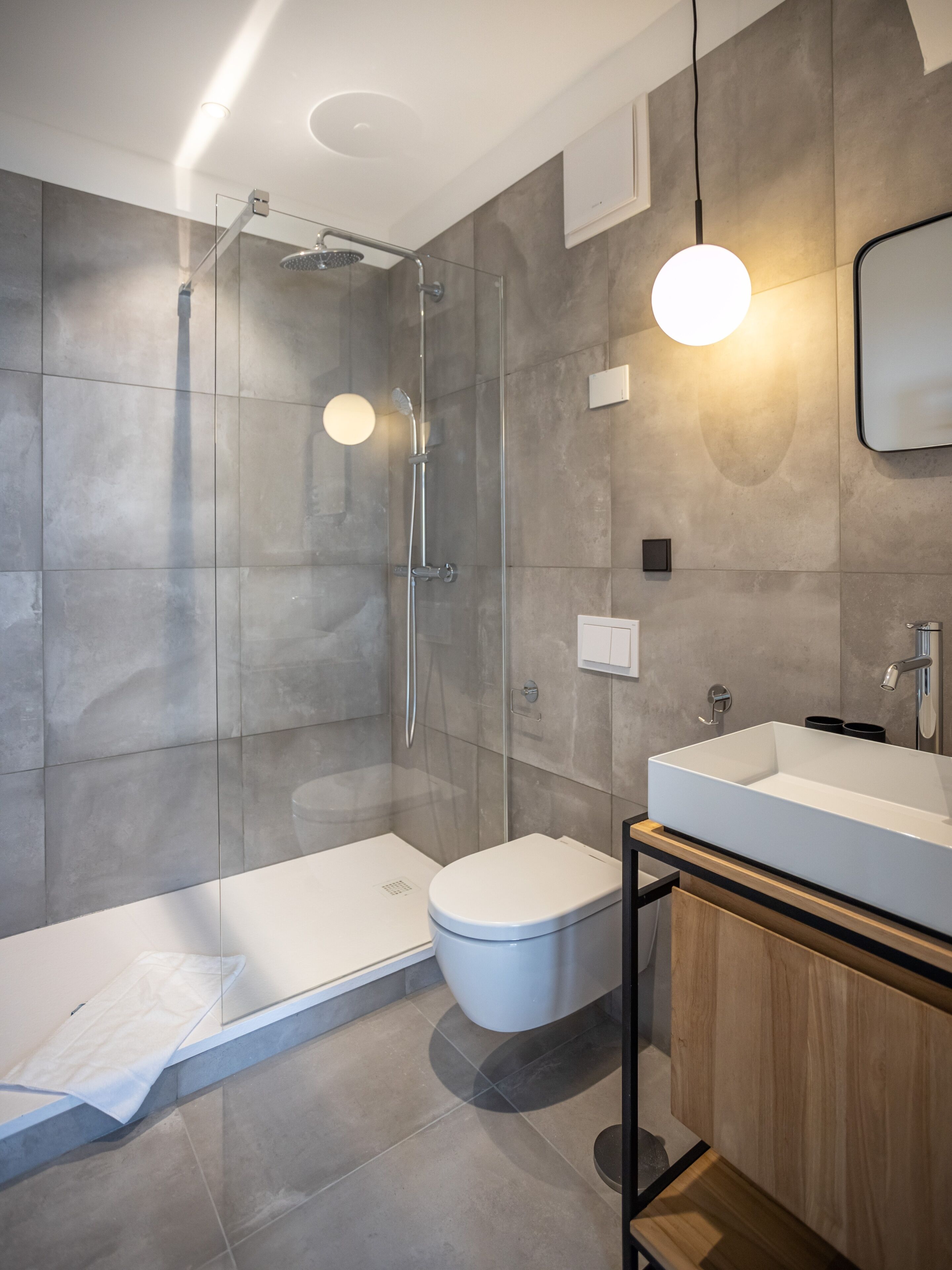 A modern bathroom with a glass-enclosed shower, a white toilet, and a wooden vanity with a large sink.