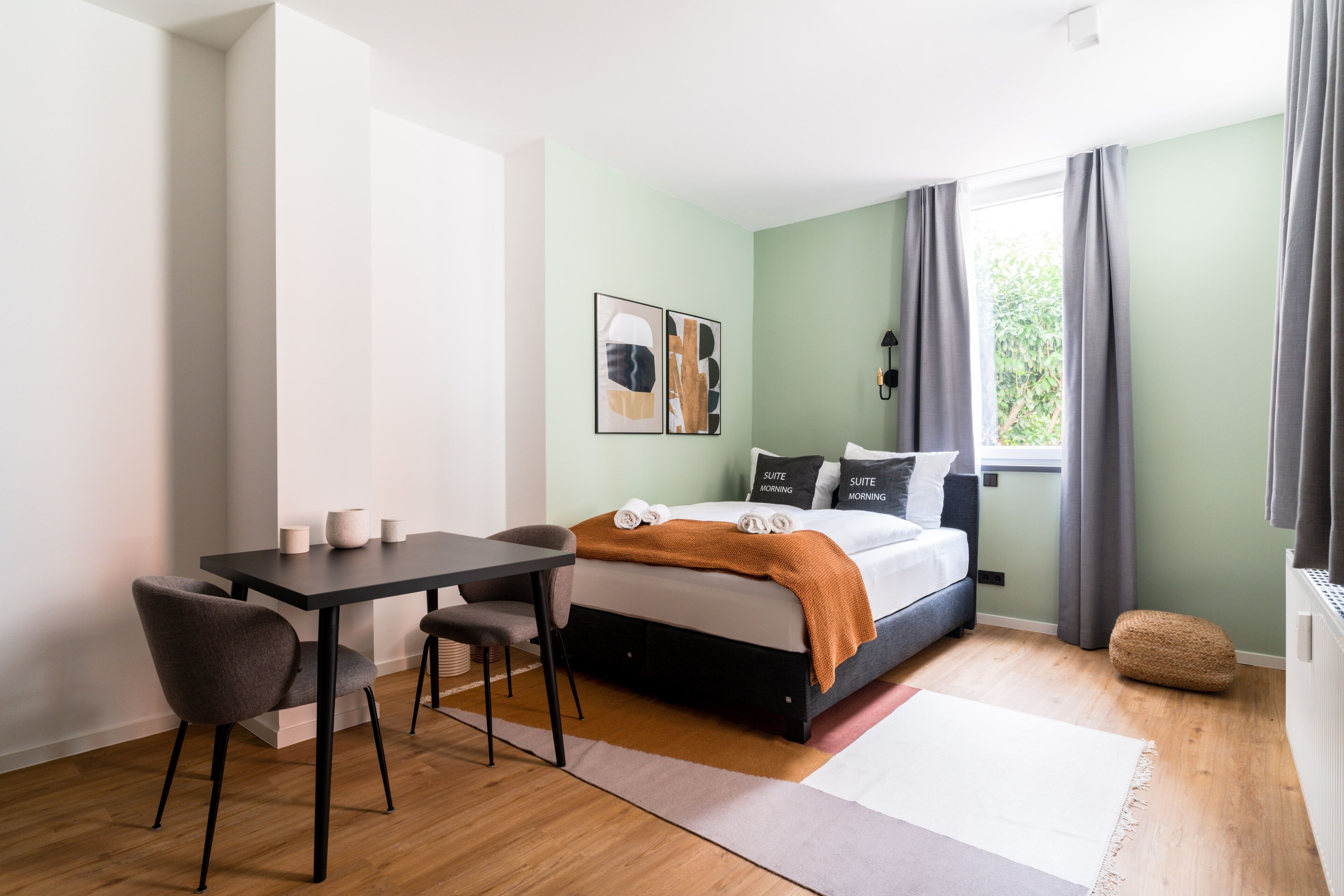 Ein modernes Schlafzimmer mit Bett, Nachttisch, Sessel und einem Fenster mit Vorhängen.