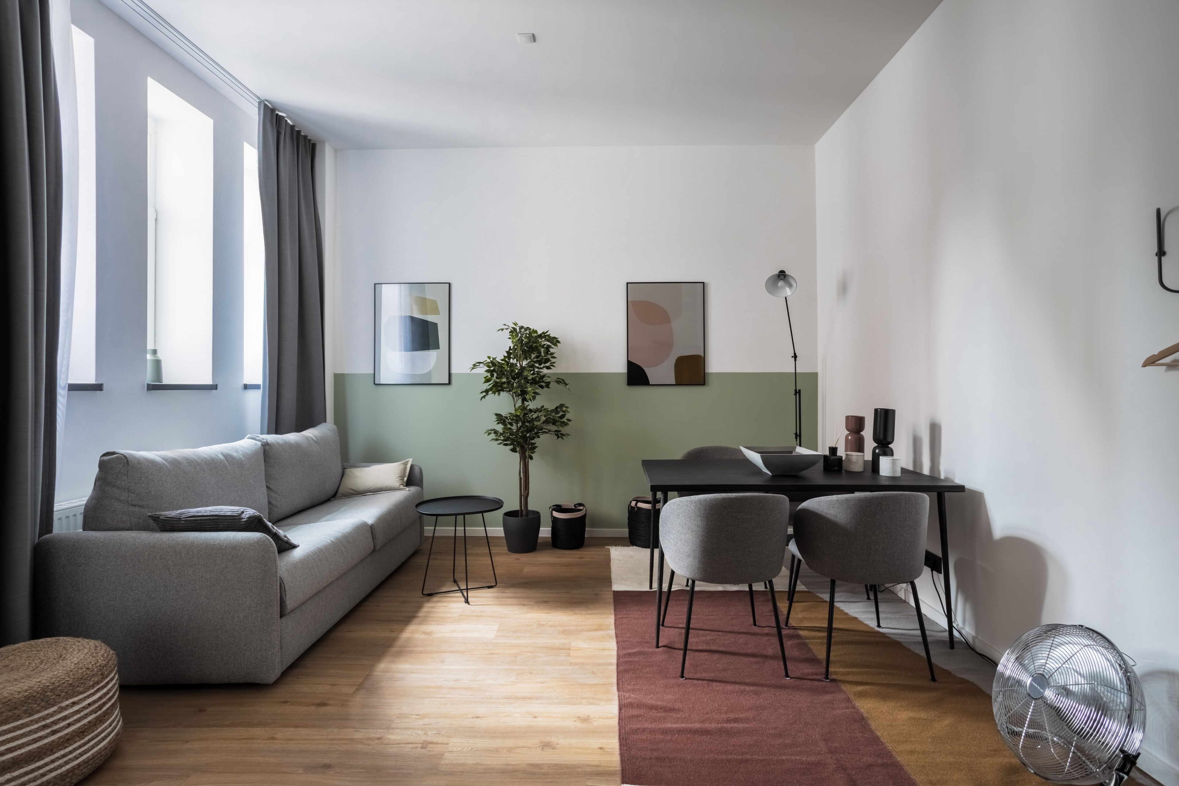A modern living room with a grey sofa, a small round table, a dining table with chairs, and a potted plant.