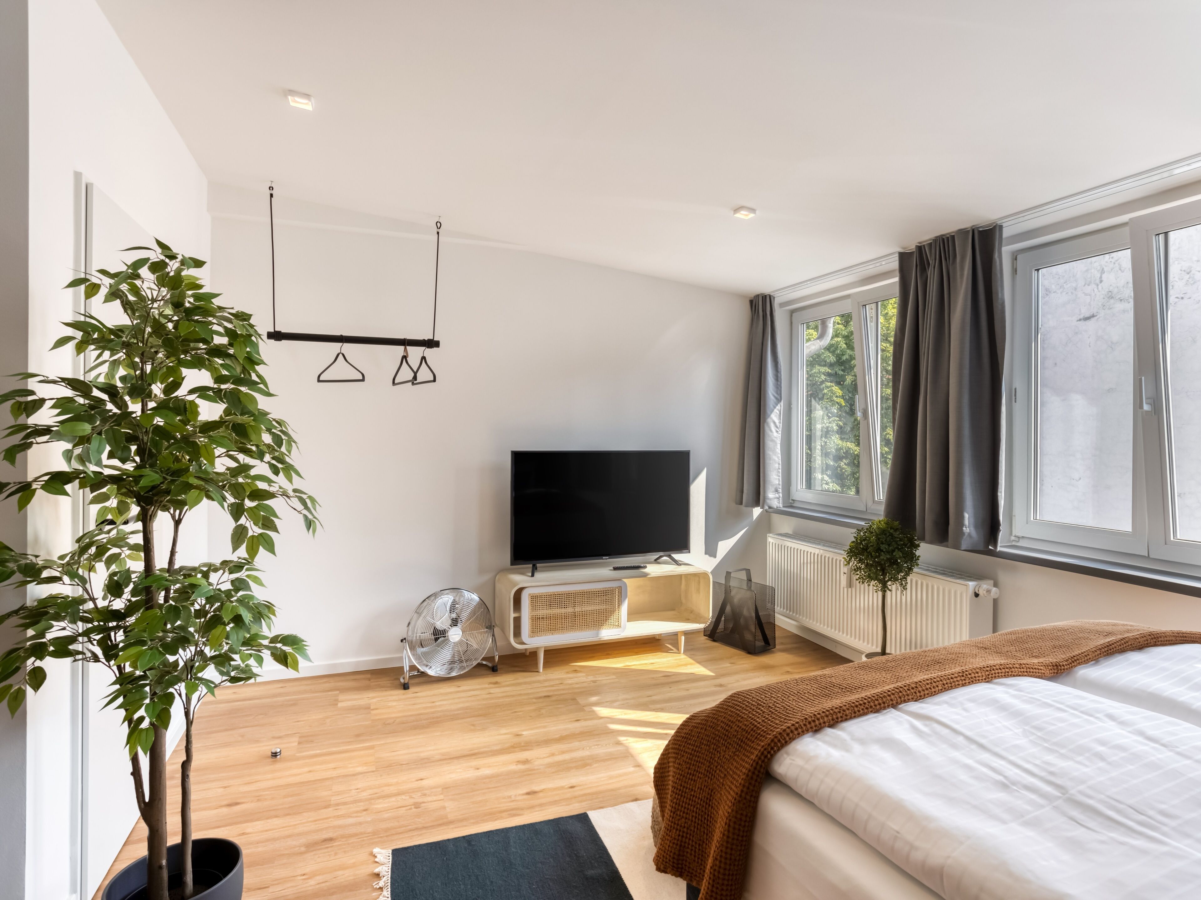 Ein modernes Schlafzimmer mit Bett, Fernseher, Heizkörper und einem Fenster mit Vorhängen.