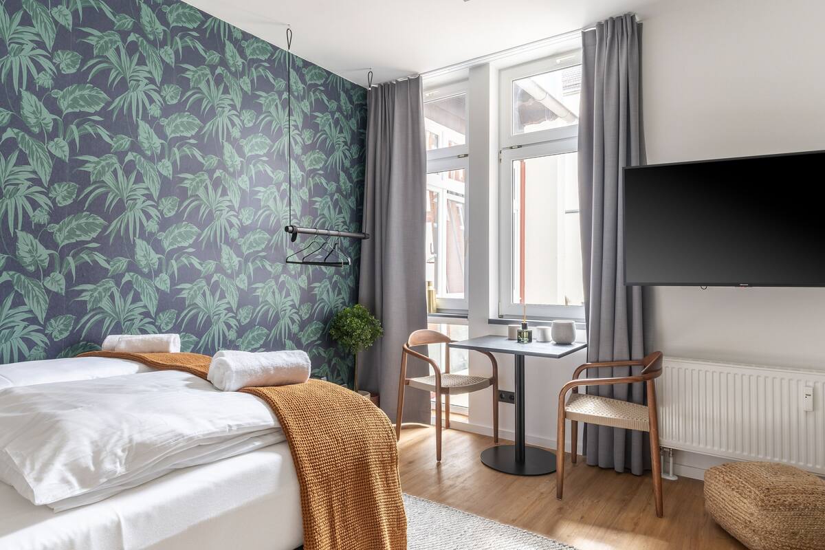 A hotel room with a bed, a table, chairs, a TV, and a window with curtains.