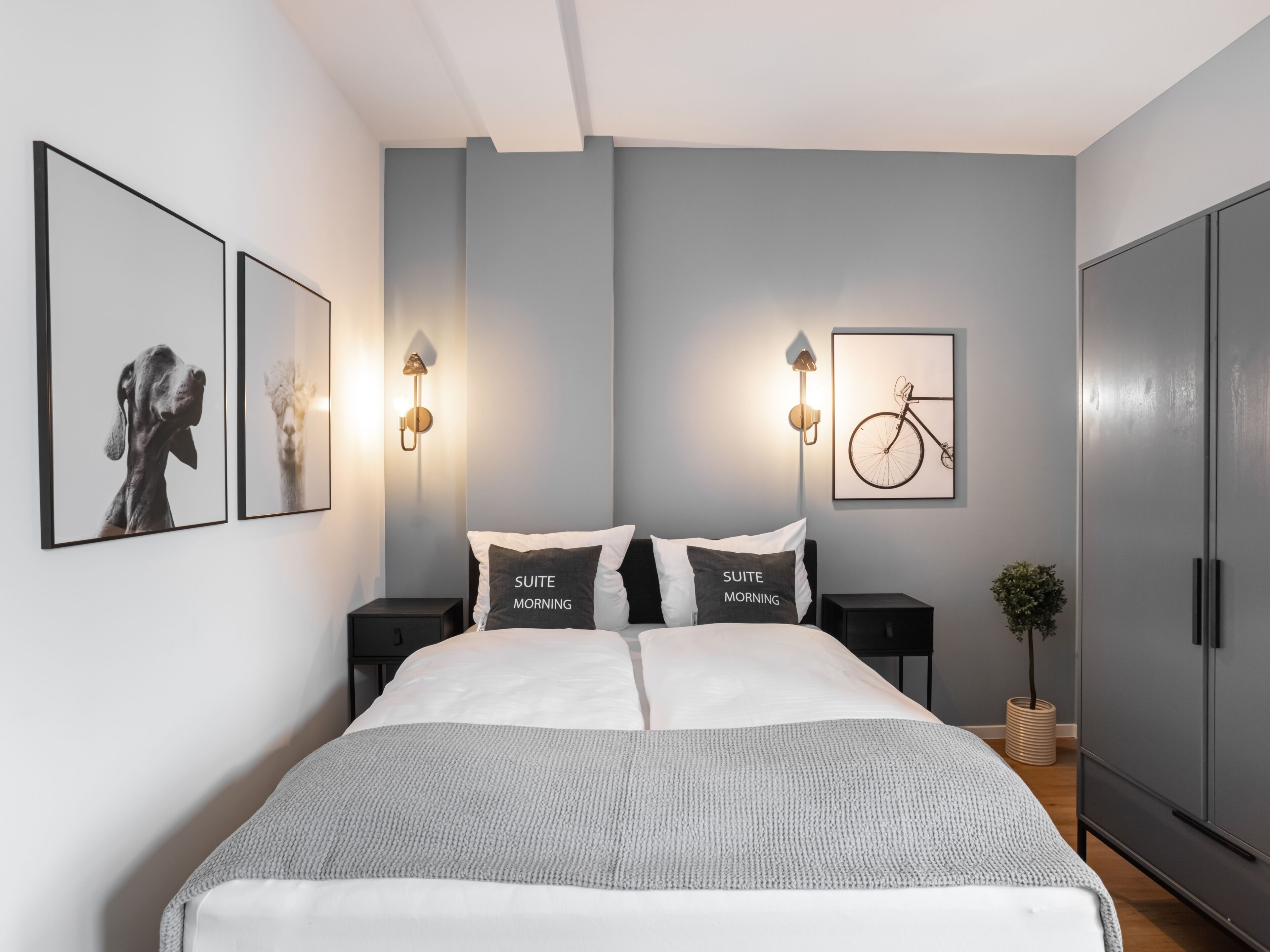 A modern bedroom with a large bed, two bedside tables, wall-mounted lights, and framed pictures.