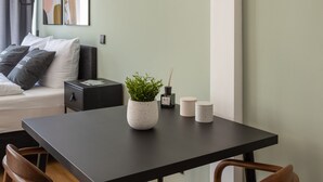 Una habitación moderna con cama, una mesa y sillas, una pequeña planta en maceta y una lámpara fijada a la pared.