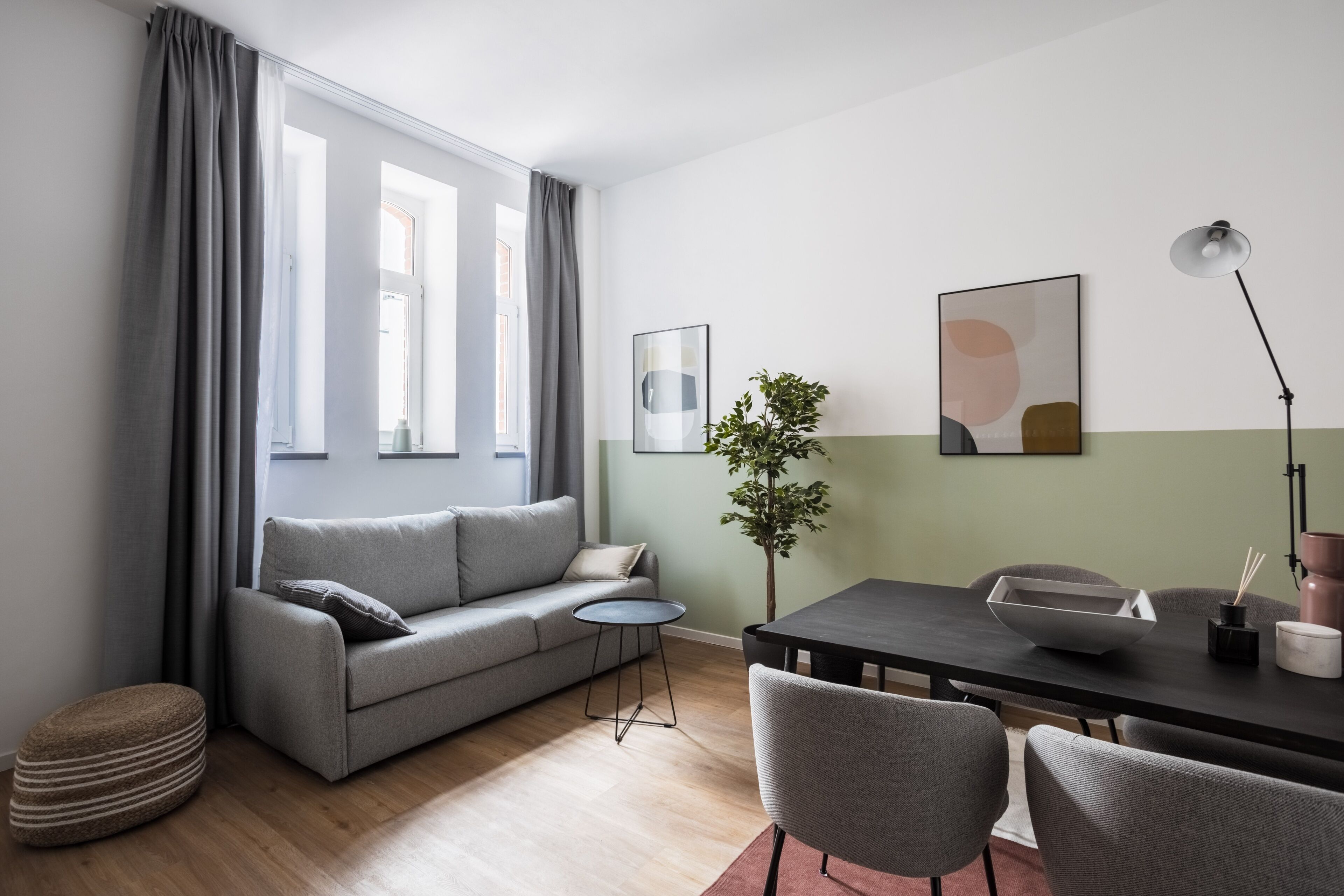 Ein modernes Wohnzimmer mit grauem Sofa, einem kleinen runden Tisch, einem Esstisch mit Stühlen und einer Kühlpflanze.