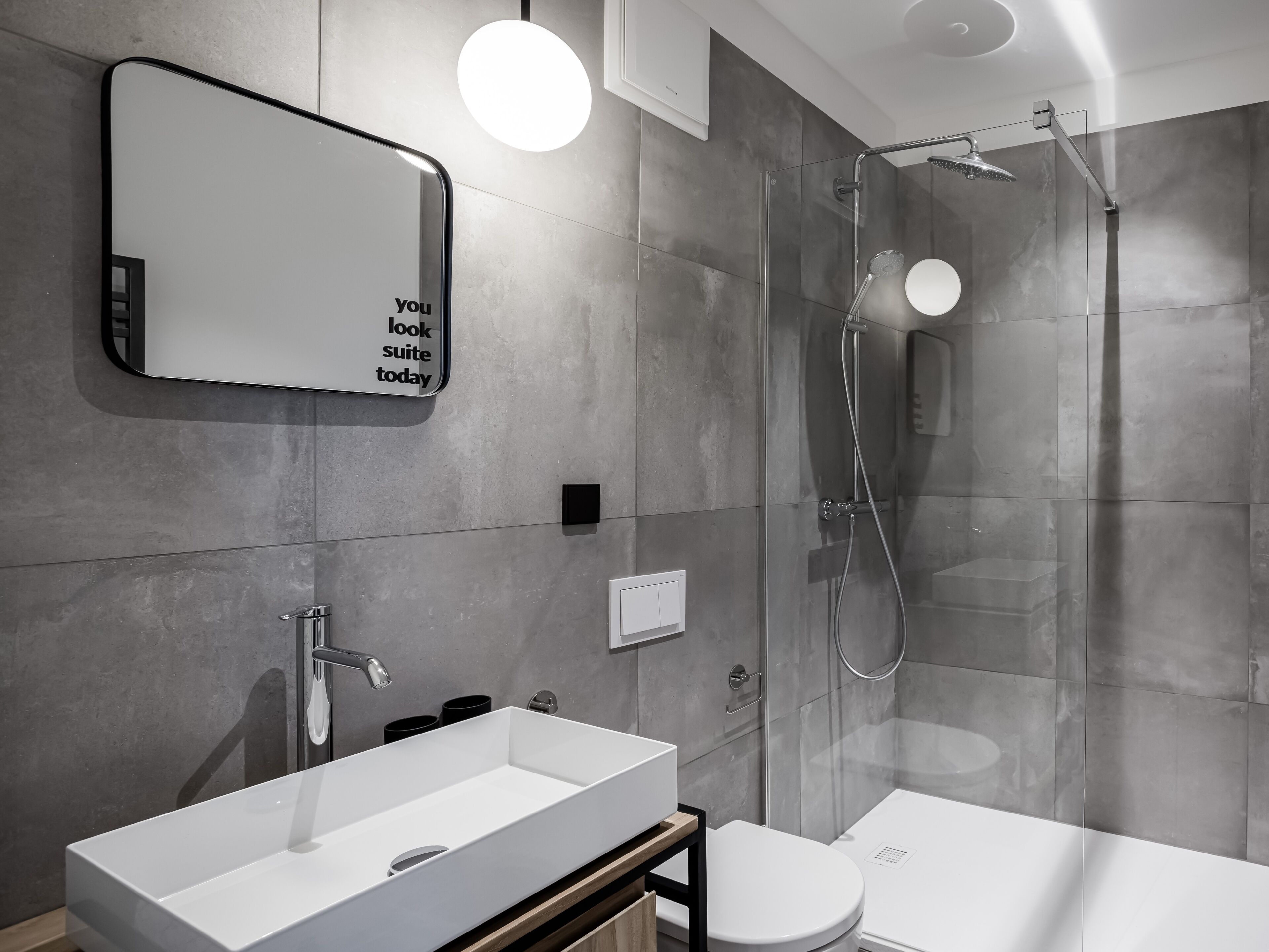 A modern bathroom with a large mirror, a white sink, and a glass-enclosed shower.