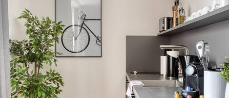 A modern kitchen with a wooden floor, a potted plant, a bicycle artwork, and a coffee machine.