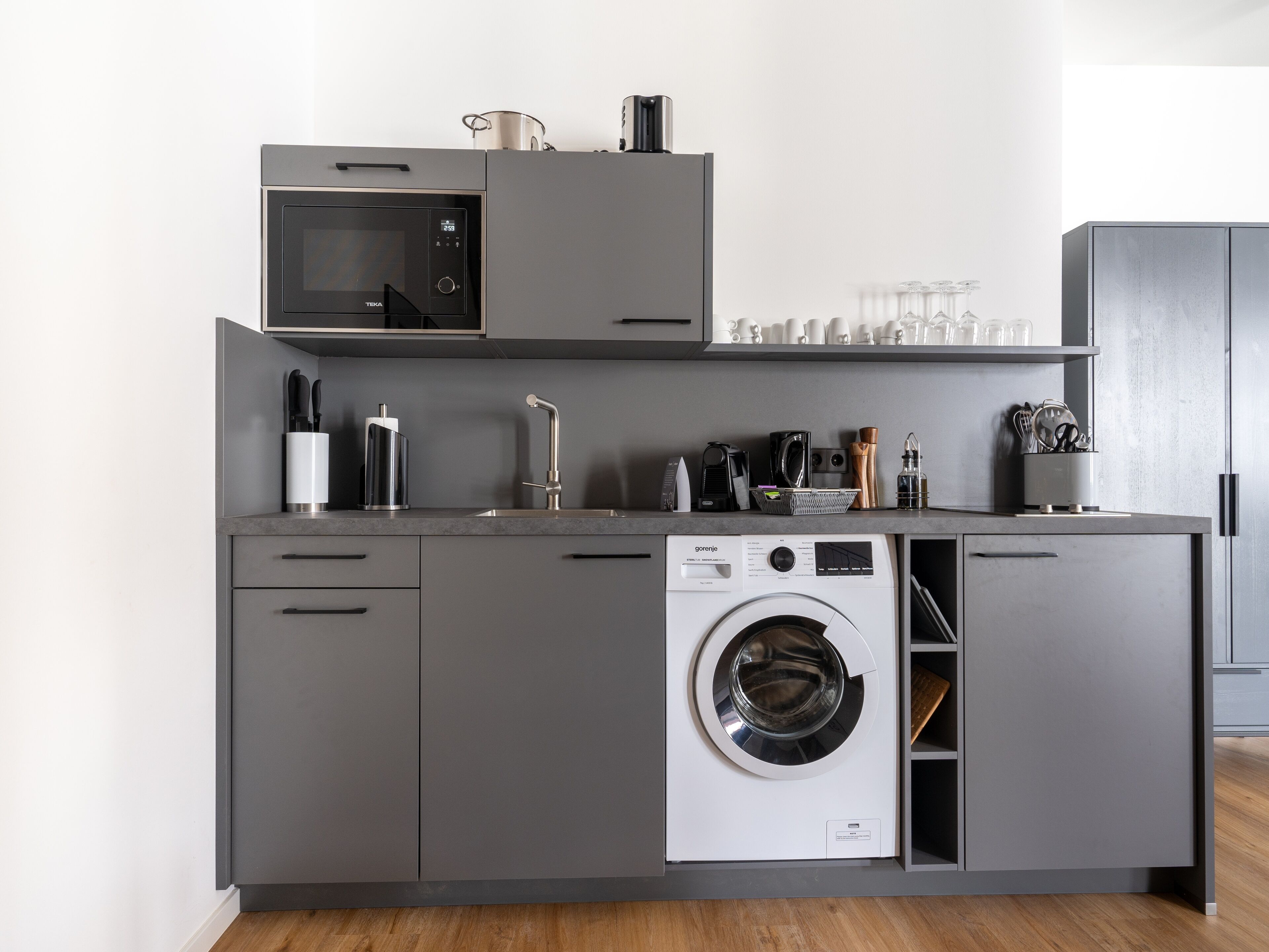 A compact kitchen with a microwave, sink, and built-in washing machine.