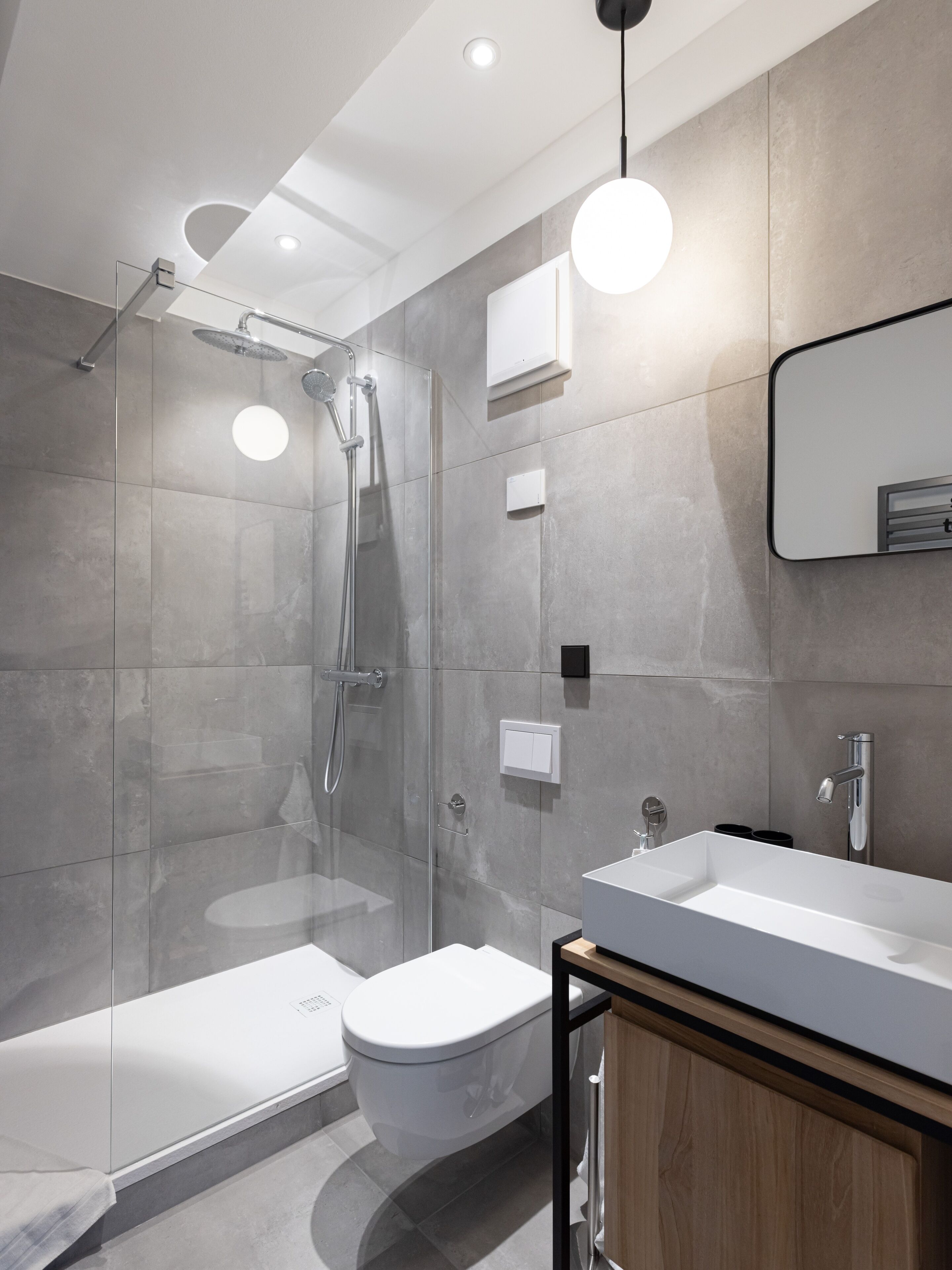 A modern bathroom with a glass-enclosed shower, a white toilet, and a wooden vanity with a sink.