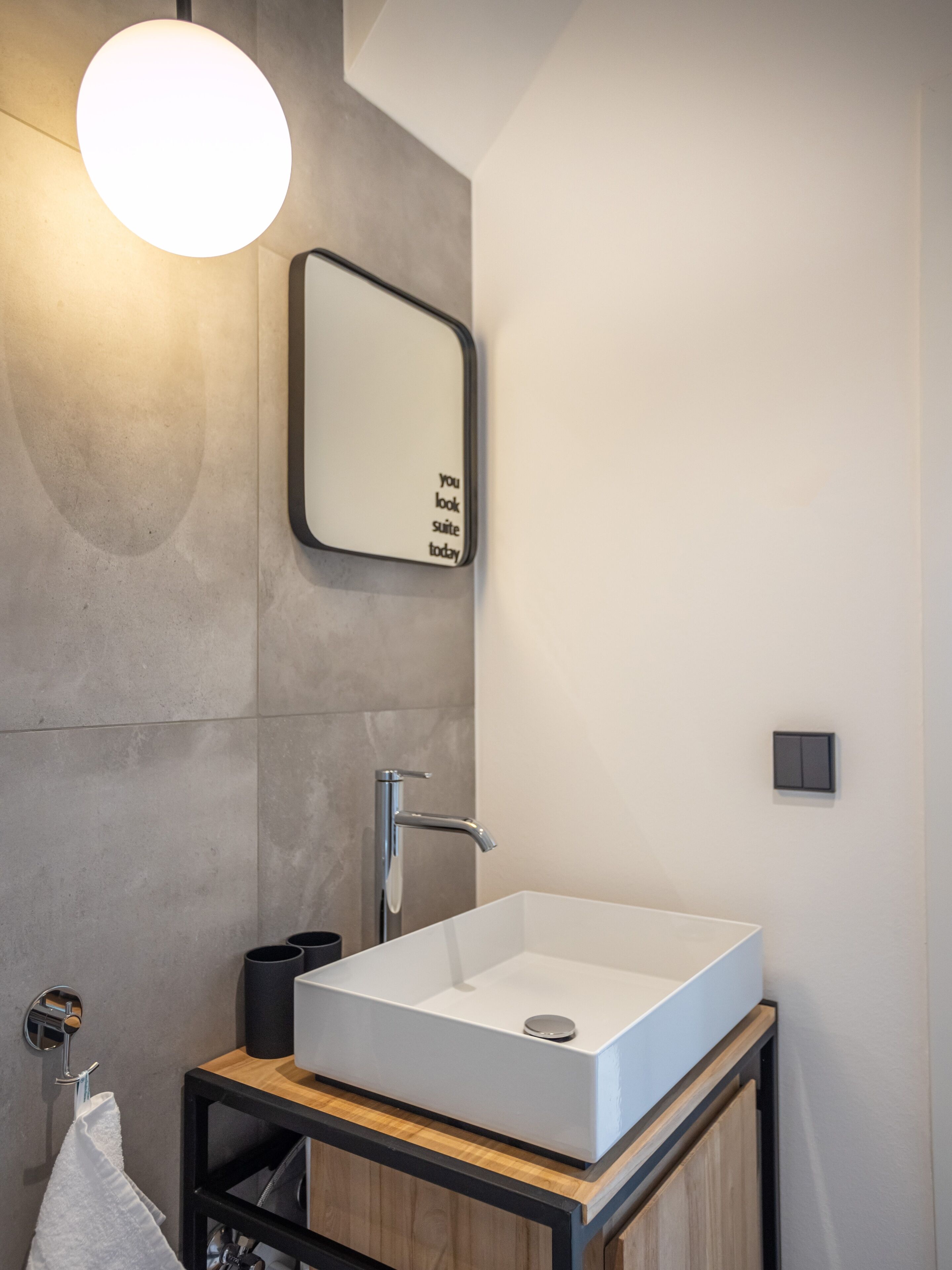 A modern bathroom with a rectangular white sink, a wall-mounted mirror, and a round light fixture.