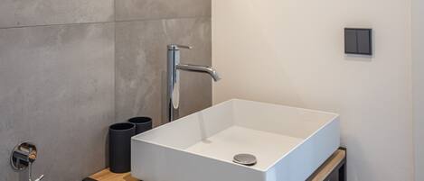 Un baño moderno con un lavamanos blanco rectangular, un espejo montado en la pared y una lámpara redonda.