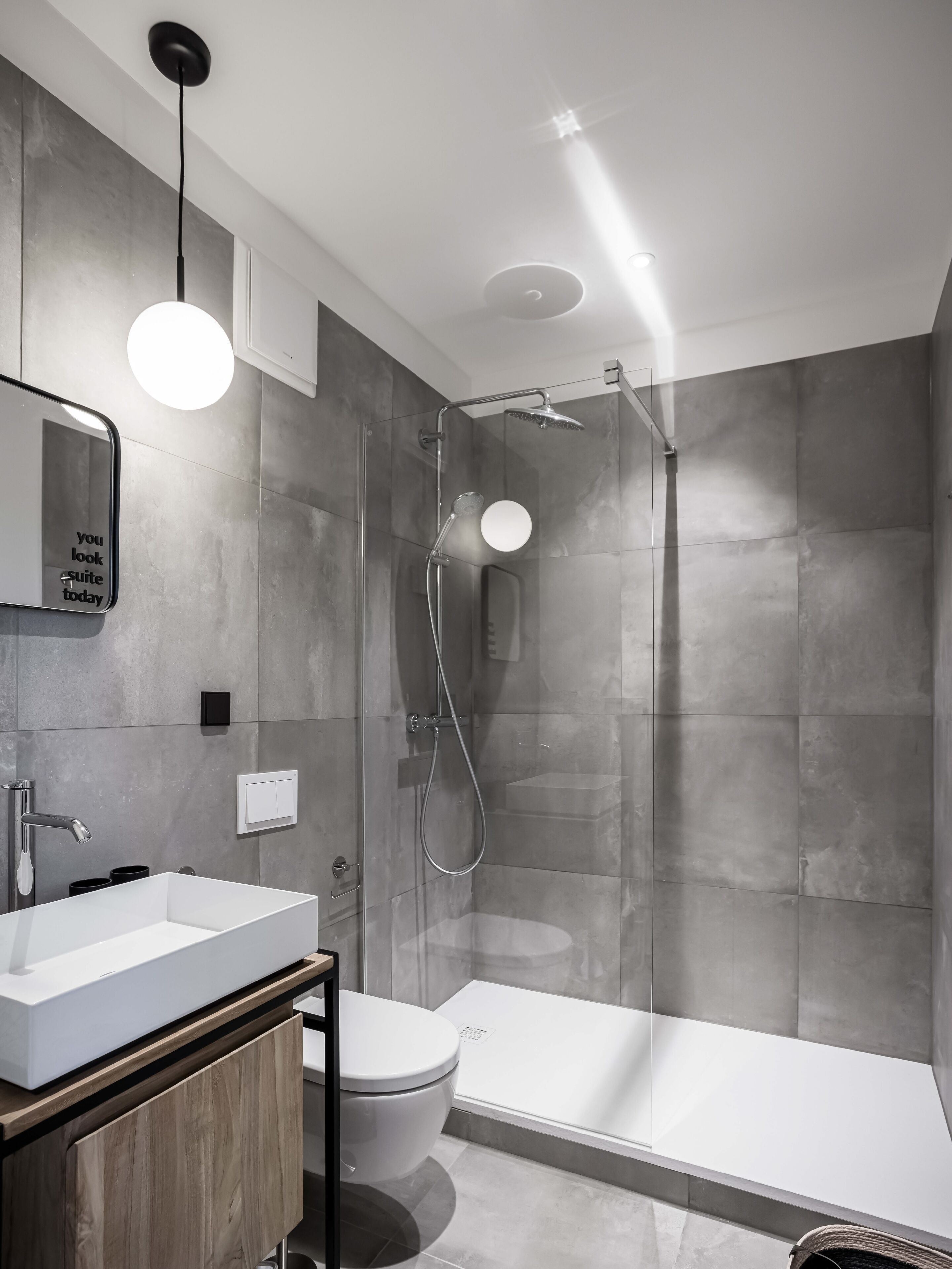 A modern bathroom with a glass-enclosed shower, a standalone toilet, and a vanity with a mirror.