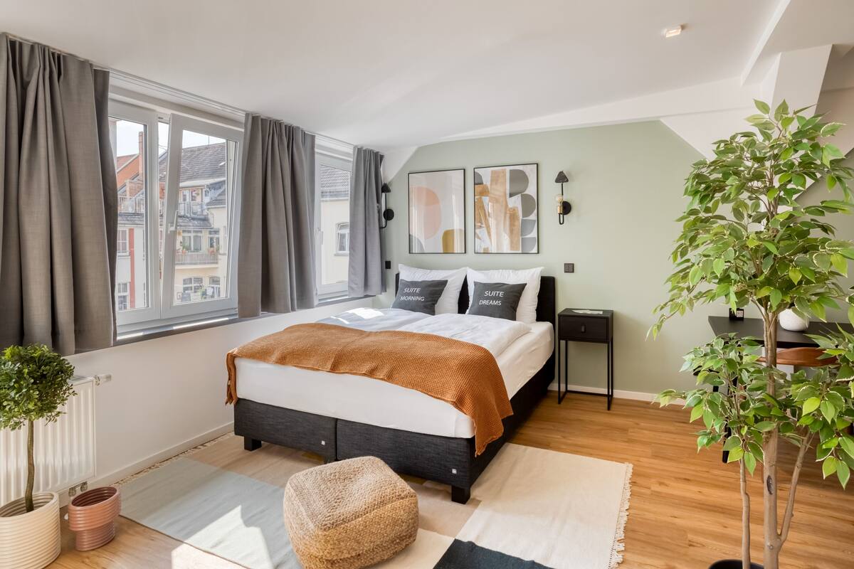 A modern bedroom with a large bed, a view of the city, and a potted plant.