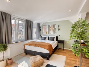 Ein modernes Schlafzimmer mit einem großen Bett, Blick auf die Stadt und einer Zimmerpflanze.