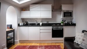 Een kleine keuken met witte kasten, een zwart aanrecht, een magnetron en een vaatwasser. Boven de gootsteen is een dakraam en er ligt een rood vloerkleed.