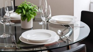 Een eettafel gedekt met borden, glazen en bestek, een potplant en een wandklok.