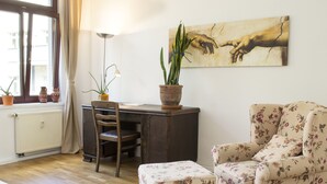 Una habitación con un escritorio de madera, una silla, un sillón estampado y una planta en maceta.