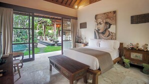 A spacious bedroom with a large bed, a wooden bench, a desk, and a view of a lush garden through large sliding doors. - Villa Avalon (Canggu)